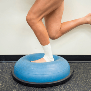 A person balances on a stability trainer during physical therapy for sprained ankle rehab sessions