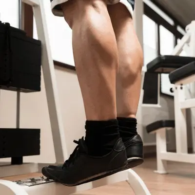 Man performing standing calf raises in a gym to strengthen lower legs and improve balance