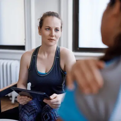 Female athlete discussing shoulder pain with a specialist during physical therapy for athletes rehabilitation session