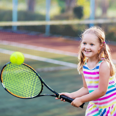 Smiling girl swings tennis racket to hit approaching ball on court during beginner practice session