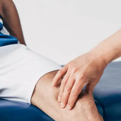 Physiotherapist assessing a patient’s knee injury during physical therapy session for muscle strain recovery