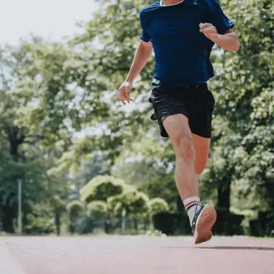 Runner in blue shirt mid-stride outdoors, demonstrating proper running form during training