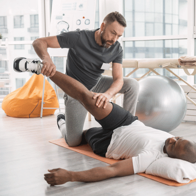 Trainer conducts functional movement screen leg assessment, lifting athlete's leg while he lies on floor