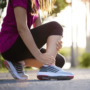 A woman grabs her ankle after jogging, needing physical therapy for sprained ankle treatment
