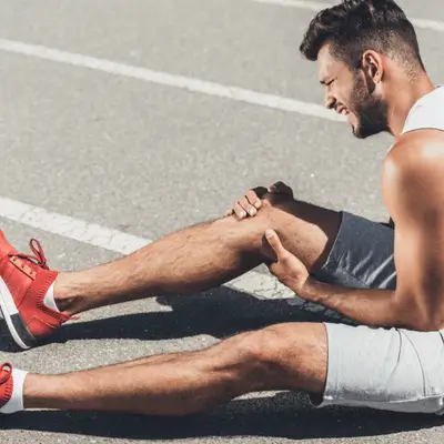 Male runner sits on track clutching painful knee, needing evaluation from physical therapist dallas soon