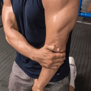 Man gripping elbow tightly, clearly affected by elbow pain when lifting at the gym