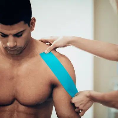 Therapist applies kinesiology tape to shoulder during orthopedic rehab to reduce strain and guide movement