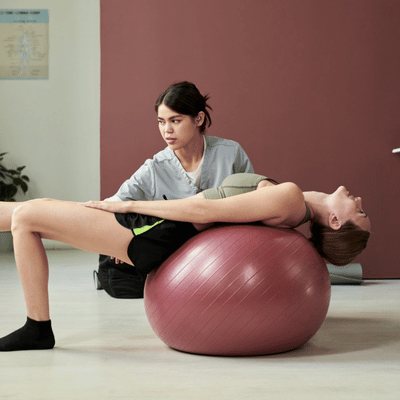Therapist guides patient on exercise ball during sports center physical therapy for core strengthening