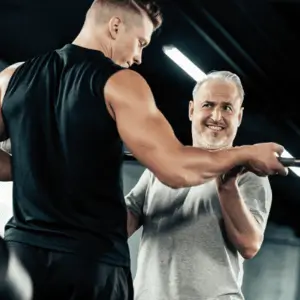 Trainer assists man with barbell to prevent elbow pain when lifting weights incorrectly