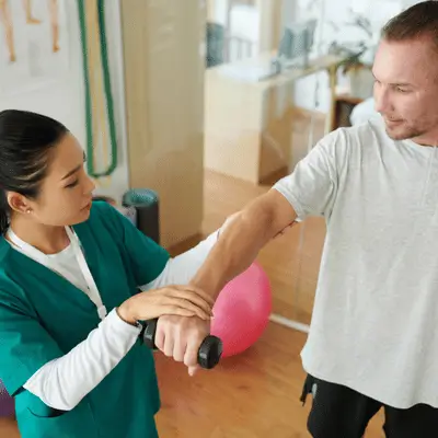 Clinician checks wrist motion while patient holds weight during orthopedic rehab session in clinic