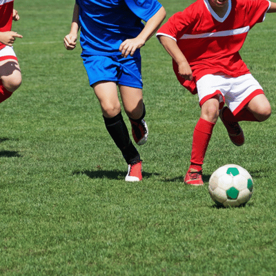 Kids sprint toward soccer ball on field, illustrating common risks for youth sports injuries today